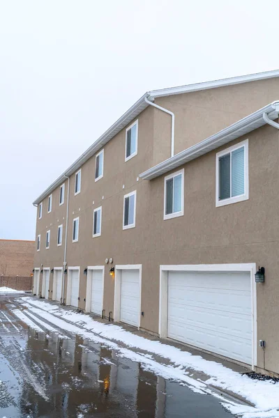 Winter on a neighborhood with wet road along white garage doors of apartments — Stock Image Winter on a neighborhood with wet road along white garage doors of apartments Royalty Free Stock Photos