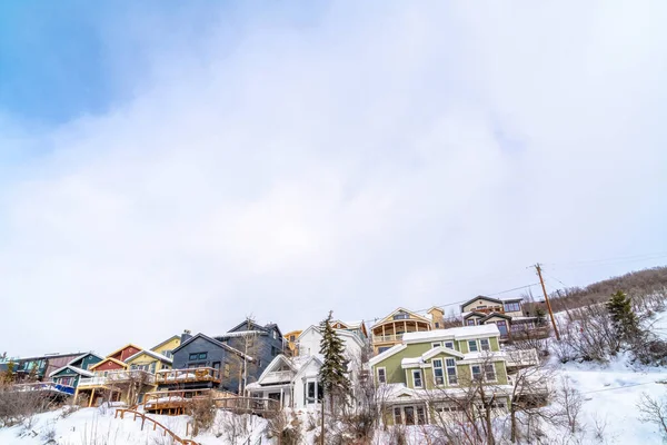Montaña con casas en pendiente cubierta de nieve bajo un paisaje de cielo azul y nubes — Foto de Stock