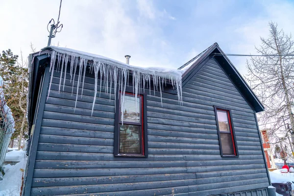 Huis met verweerd hout buitenmuur en scherpe ijspegels voering van het besneeuwde dak — Stockfoto