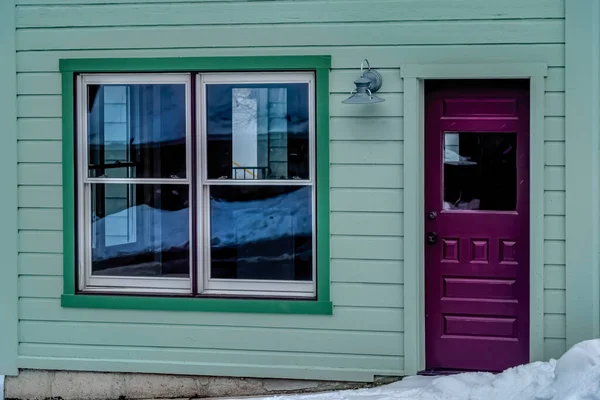 Glass paned purple front door and single hung windows at facade of green home