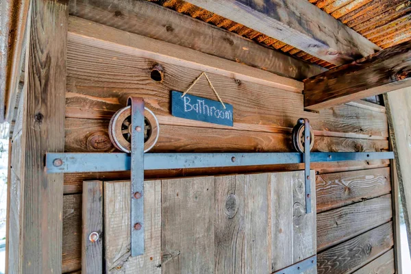 Rustykalna łazienka na zewnątrz z przesuwanymi drewnianymi drzwiami i zardzewiałym dachem falistym — Zdjęcie stockowe