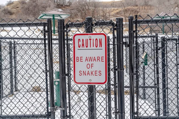 Precaución Tenga en cuenta el signo de serpientes en la cerca de eslabones de cadena de un parque recreativo — Foto de Stock