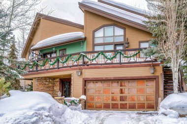 Evin önünde karlı bahçe ve garaj yolu var. Ön kapıda metal garaj kapısı var.