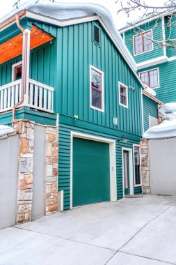 Yeşil dış duvarı ve kışın yoğun karla kaplı çatısı olan ev.