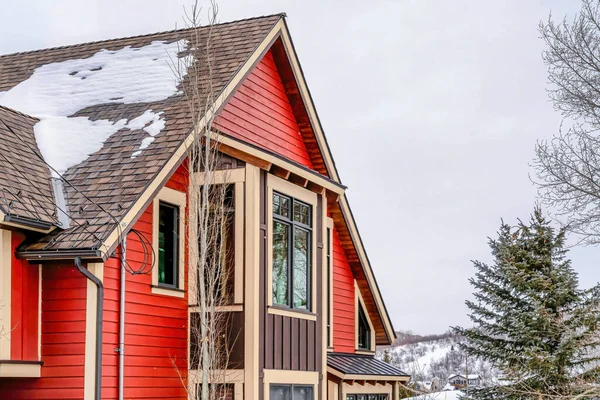 Home with snowy pitched roof over bay window and vibrant red exterior wall