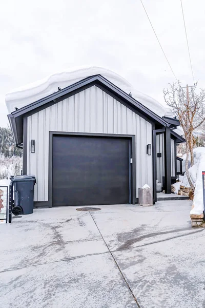 Garaje de la casa con techo a dos aguas cubierto de nieve y puerta gris oscuro contra la vista al cielo nublado — Foto de Stock