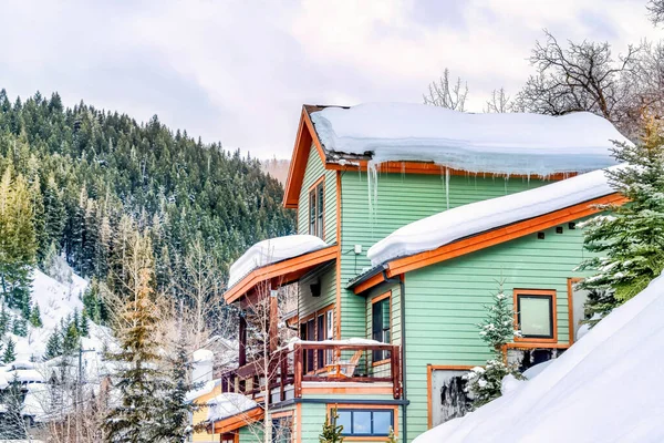 Home with green wall and balcony overlooking snowy hill and lush evergreens — Stock Photo, Image