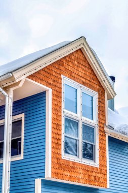 Evin dış yüzeyi kahverengi yuvarlak kiremitli ve mavi yatay kaplamalı.