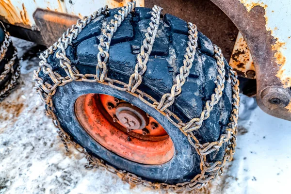 Enormt svart hjul av en bulldozer insvept med rostiga kedjor mot snö — Stockfoto