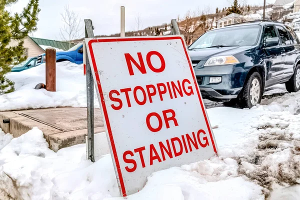 No Stopping or Standing sign on snowy land against vehicles ona parking lot