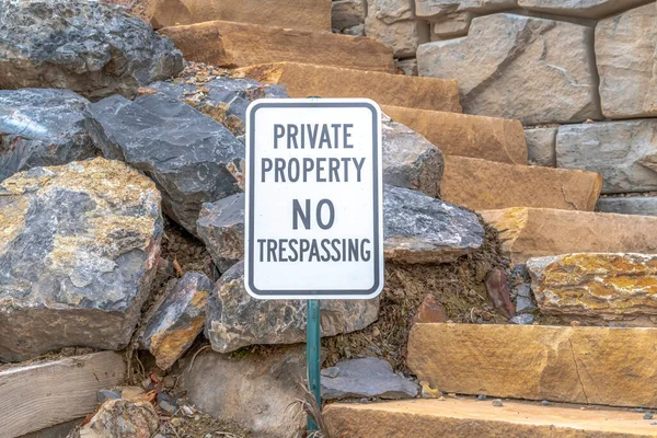 Private Property No Trespassing sign against jagged rocks and stone stairway