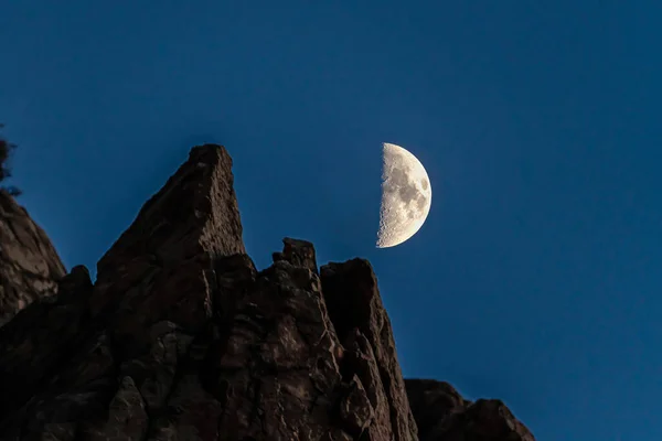 Half moon and rocky mountain in Provo Canyon against dark blue sky at night
