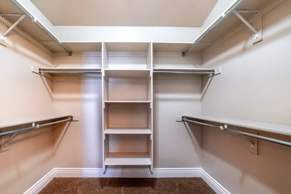 Walk in closet with empty storage shelves for clothes built against white wall — Stock Photo, Image