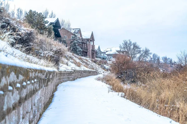 Camino cubierto de nieve en invierno a lo largo de una pendiente con casas y muro de contención — Foto de Stock