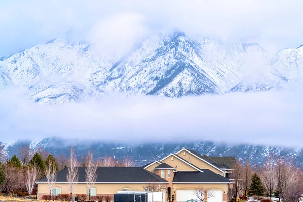 Home fachada contra majestosa montanha nevada parcialmente escondida por nuvens no inverno — Fotografia de Stock