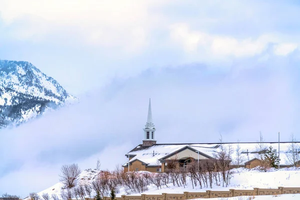 Церковь в пригороде против снежной горы, частично скрытой облаками — стоковое фото