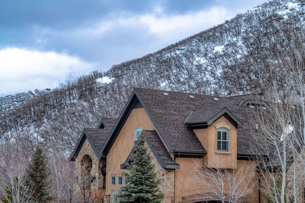 Home with gable roofs and stone exterior wall against snowy hill and cloudy sky