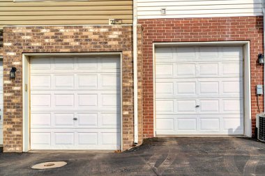 Beyaz panelli garaj kapıları. Duvarında tuğla ve ahşap kaplama var.