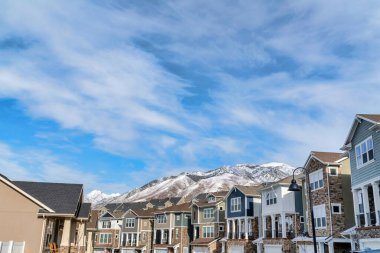 Karlı dağ zirvesi ve bulutlu mavi gökyüzü kışın evlerin arkasında.