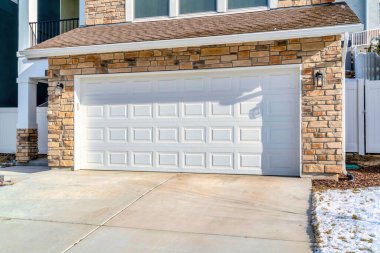 Taş duvarlı bir evin garajının geniş beyaz garaj kapısı.