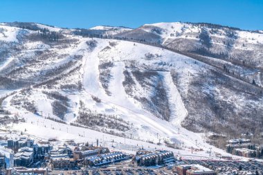Park City Utah dağında kışın karlı bir manzarada kayak yolları ve binaları var.