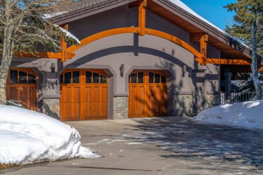 Üç cam camlı ahşap garaj kapısına çıkan asfalt kapaklı ev cephesi.