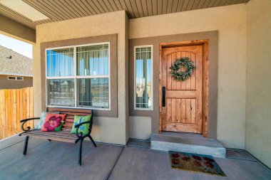 Açık verandalı, kahverengi ahşap kapılı, neşeli çelenkli bir ev cephesi.