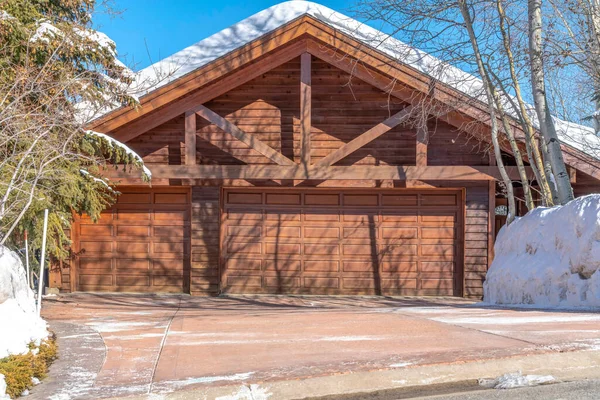 Karlı çatılı ve kahverengi ahşap dış duvarlı ev garajı cephesi.