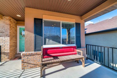 Evin ön verandasında güneş ışığı, pencereli ahşap bir bank ve kepenkler.