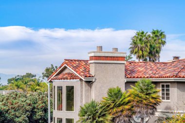 House exterior with tile roof bow bay window and chimney against clouds and sky