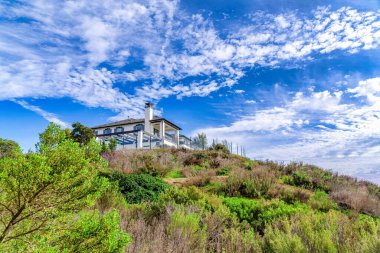 House sitting on a slope against vibrant cloudy blue sky in Huntington Beach