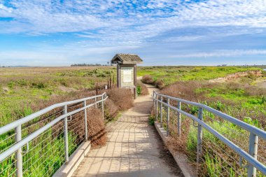 Pathway with railing and sign board with roof on grass land in Huntington Beach