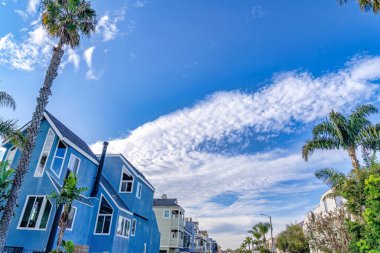 Looking up to vibrant blue sky with puffy clouds over houses in Huntington Beach