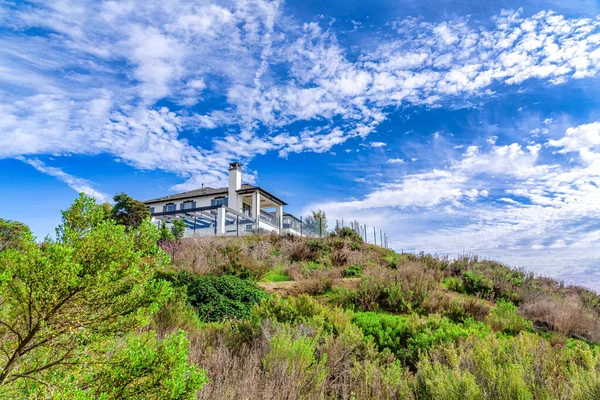 House sitting on a slope against vibrant cloudy blue sky in Huntington Beach