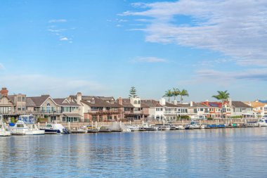 Houses in Huntington Beach bordering sea with reflection of clouds and blue sky