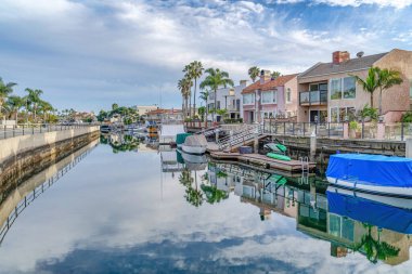 Road and homes bordering the canal with boats and reflection of overcast sky