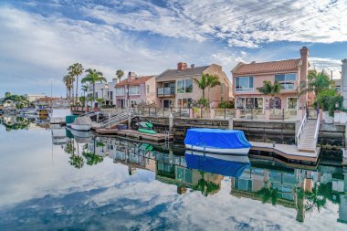 Blue sky and clouds reflected on water of canal bordered by houses and docks