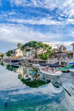 Boats on harbour reflecting trees and cloudy blue sky in Huntington Beach CA