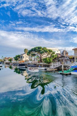 Clear water reflecting clouds and blue sky bordered by homes in Huntington Beach