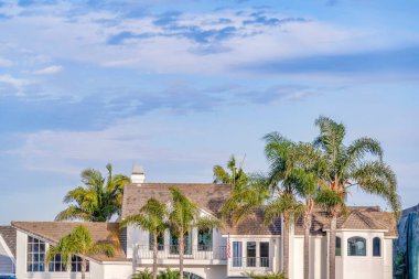 Luxury house exterior view and tall palm trees against blue sky with clouds