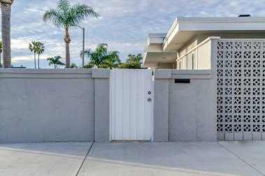 White gate and concrete fence agaonst trees and cloudy sky of beautiful home