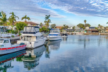 Yachts on serene water that reflects the cloudy blue sky in Huntington Beach CA