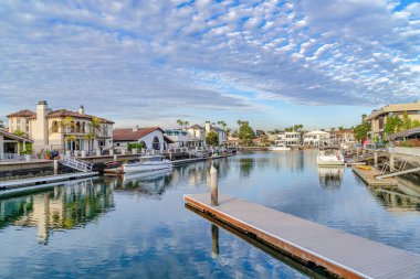 Boats and private docks on sea reflecting cloudy blue sky in Huntington Beach CA