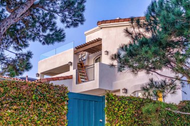 Mavi kapı ve çit, sarmaşıklı ev, balkon ve beyaz dış duvar.