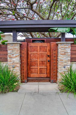 San Diego California 'da tuğla direkleri ve çitlere karşı çatılı kahverengi ahşap kapı.