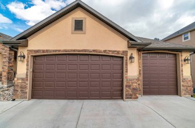 Bulutlara ve mavi gökyüzüne karşı eve bağlı iki araba garajının ön görüntüsü