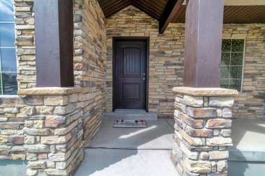 Açık tuğla duvarlı, koyu kahverengi ahşap ön kapılı, güneşli ev cephesi.