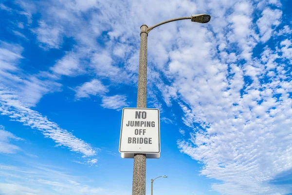 No Jumping Off Bridge znak na latarni przed niebieskim niebem i chmury puszyste — Zdjęcie stockowe