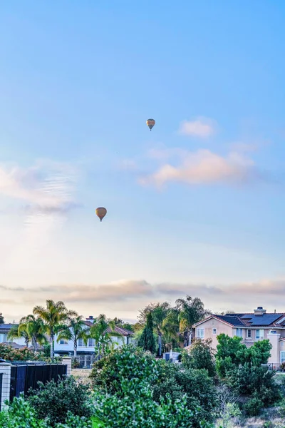 Warme lucht ballonnen vliegen over huizen en bomen met blauwe lucht en wolken achtergrond — Stockfoto