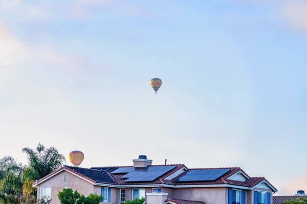Palloncini colorati aria calda contro cielo blu nuvoloso sopra casa con pannelli solari — Foto Stock